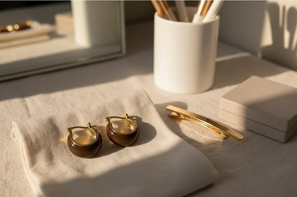 Brown Resin Huggie Hoop Earrings on fabric by vanity mirror and makeup brushes | OriaJewel