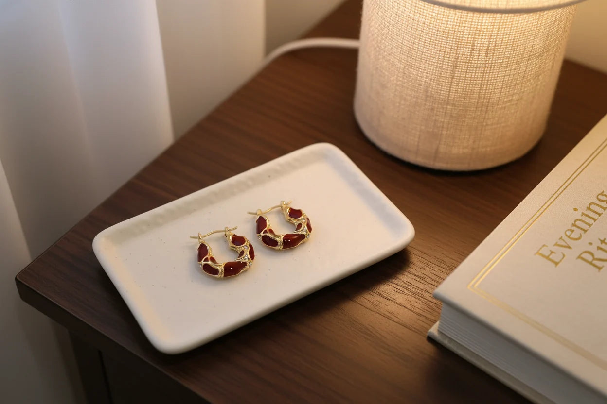 Burgundy Huggie Hoop Earrings on tray beside lamp and book | OriaJewel