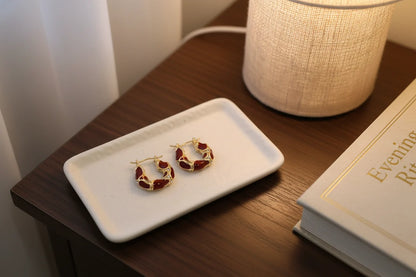 Burgundy Huggie Hoop Earrings on tray beside lamp and book | OriaJewel