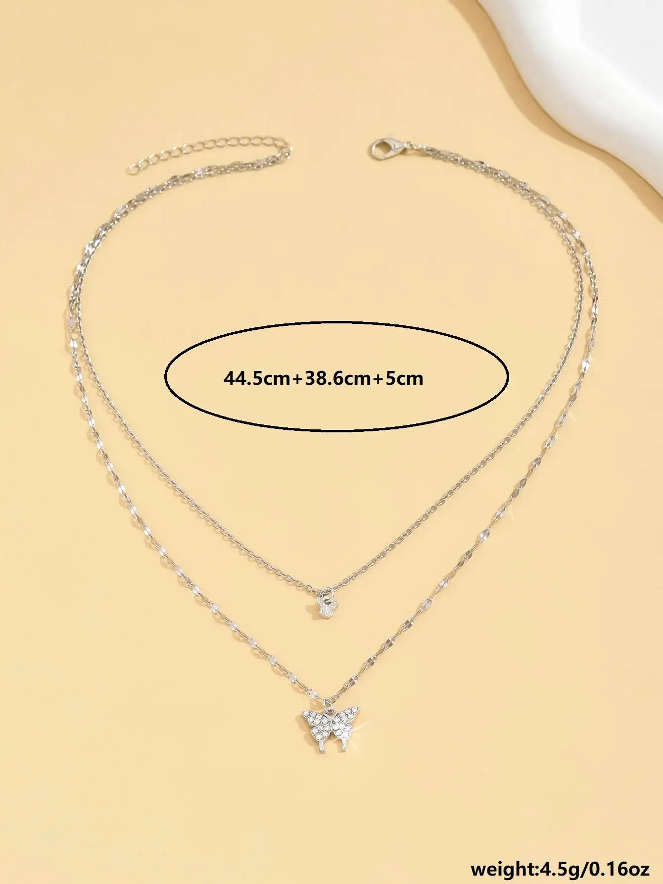 Product shot of the Butterfly Layered Necklace on a beige background with measurements text showing 44.5cm + 38.6cm + 5cm and weight 4.5g to highlight size details | Oria Jewel