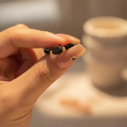 Hand holding a black Cat Charm Ring with gold beads in soft light | Oria Jewel