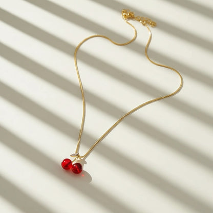 Cherry Pendant Necklace with gold chain and twin red charms displayed under striped sunlight on cream background | Oria Jewel