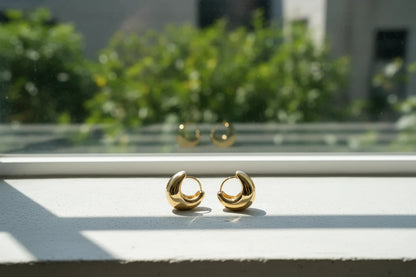 Chunky Gold Huggie Hoop Earrings on sunlit windowsill with greenery bokeh | OriaJewel