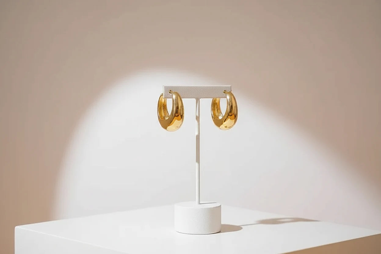 Chunky Gold Huggie Hoop Earrings on white stand with soft spotlight | OriaJewel