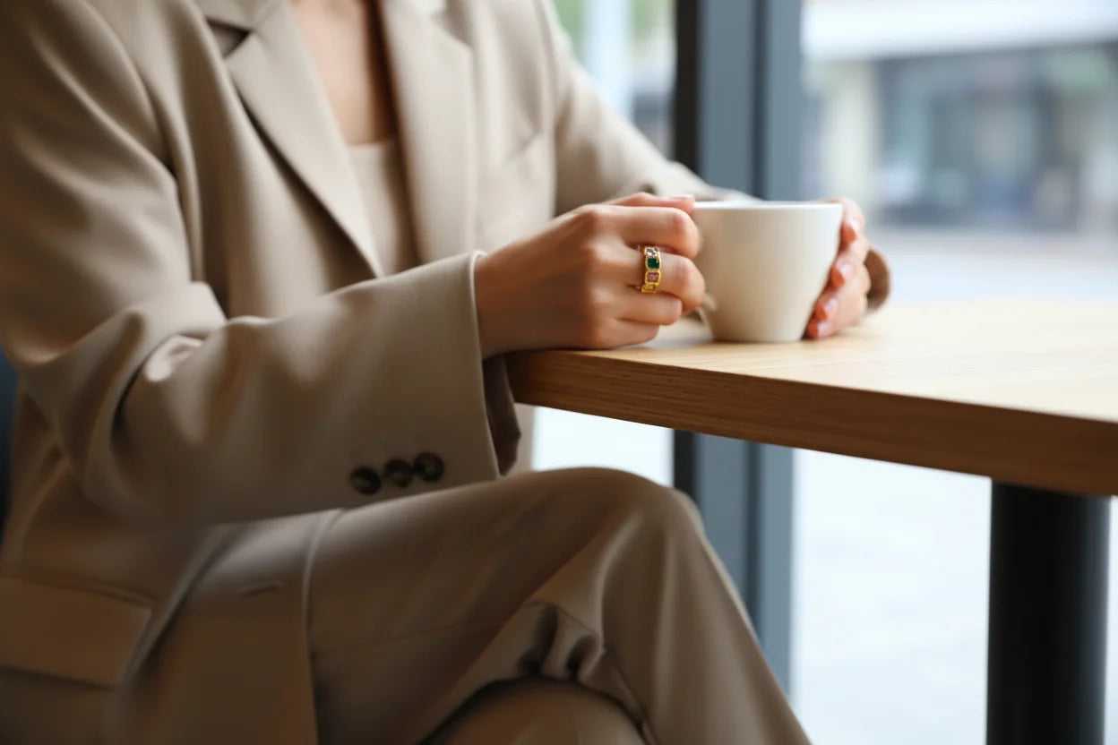 Cozy café moment holding a cup, showcasing a Colorful stone band ring with vibrant bezel-set stones | OriaJewel