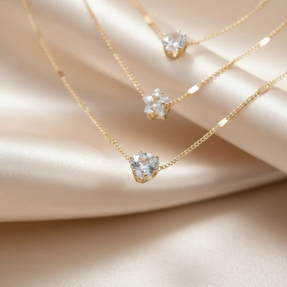 Close-up of Cosmic Star Necklace in gold showing three sparkling star-shaped pendants on delicate layered chains over beige satin | Oria Jewel