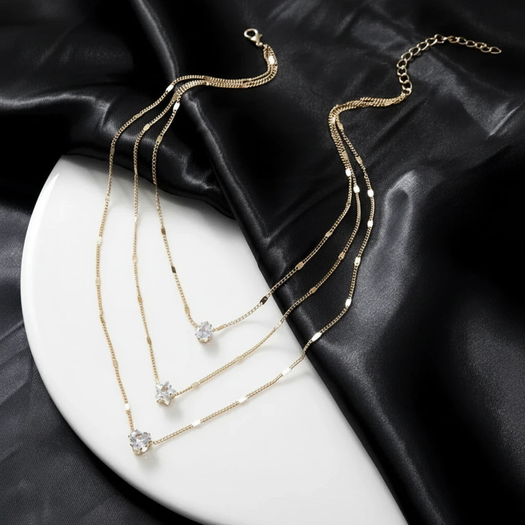 Cosmic Star Necklace in gold with triple star pendants displayed on elegant black satin and white ceramic plate | Oria Jewel