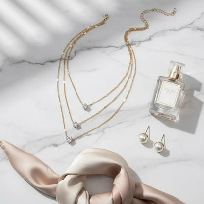 Cosmic Star Necklace in gold arranged with pearl earrings, satin ribbon, and perfume on bright marble tabletop | Oria Jewel