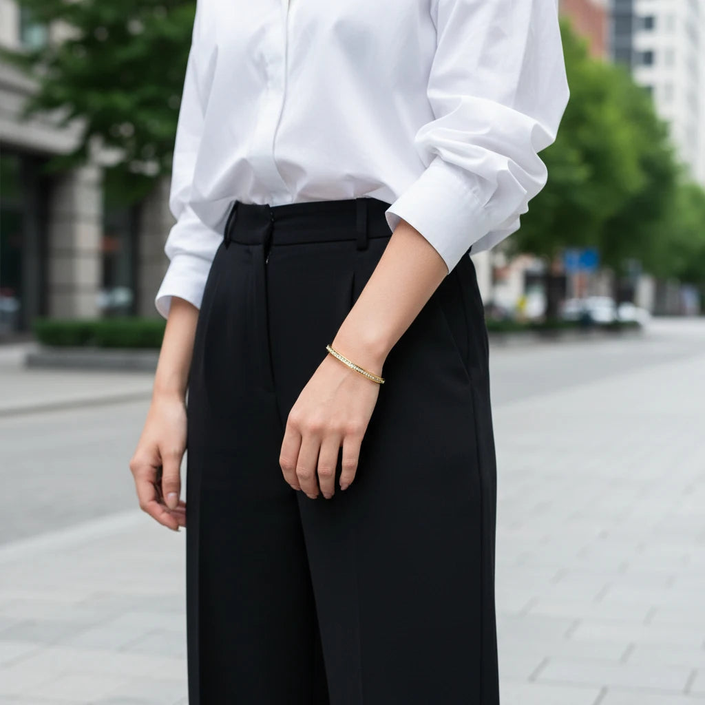 Woman in a crisp white shirt and tailored black trousers wearing the Crystal Line Gold Bangle on her wrist while walking in the city, showing how the slim crystal bracelet adds a subtle luxury accent to a modern work outfit | Oria Jewel