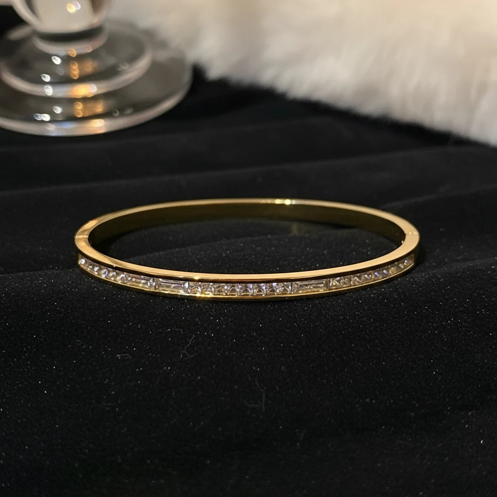 Crystal Line Gold Bangle displayed on black velvet with a glass detail in the background, the slim gold bracelet forming a perfect circle with a continuous channel of clear crystals for a classic evening-ready sparkle | Oria Jewel