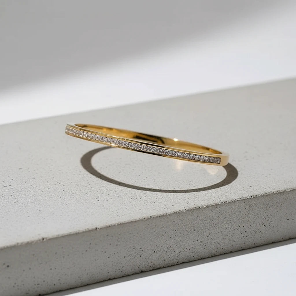 Crystal Line Gold Bangle placed on a light concrete block with strong shadows, the fine row of pave-style crystals and slim gold profile showcased in an architectural, modern product shot | Oria Jewel
