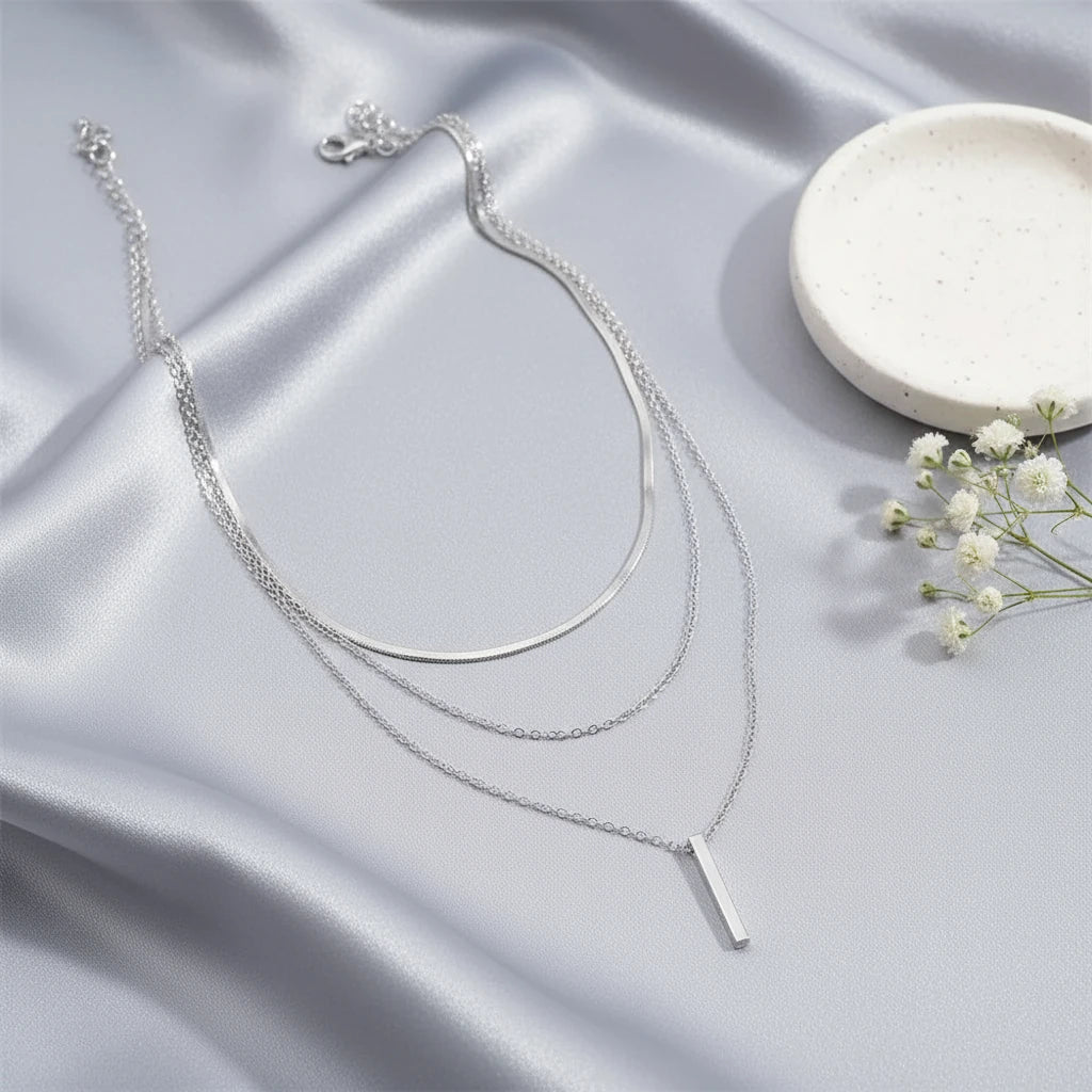 Drop Bar Pendant Necklace in silver displayed on smooth satin fabric beside white flowers and ceramic plate | Oria Jewel