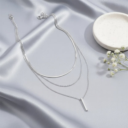 Drop Bar Pendant Necklace in silver displayed on smooth satin fabric beside white flowers and ceramic plate | Oria Jewel