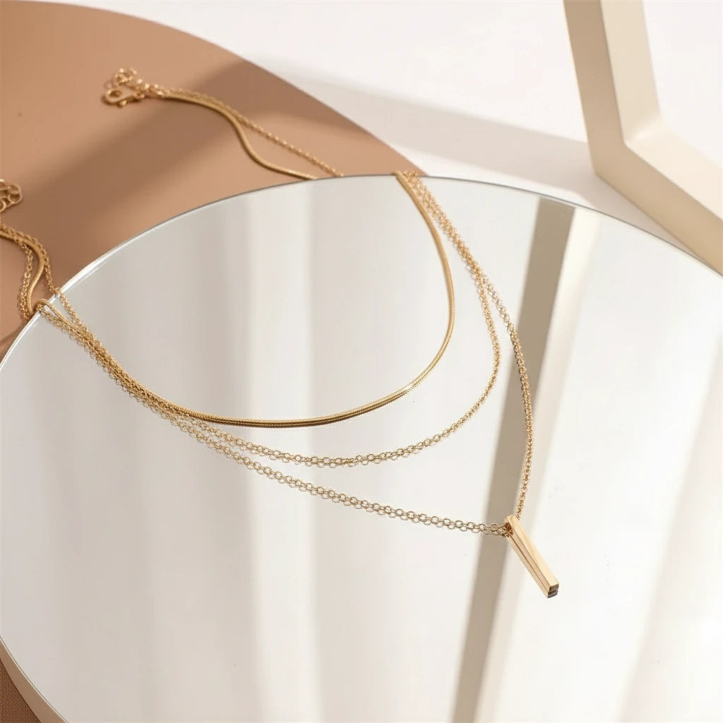 Drop Bar Pendant Necklace in gold elegantly layered on reflective mirror surface under soft natural lighting | Oria Jewel
