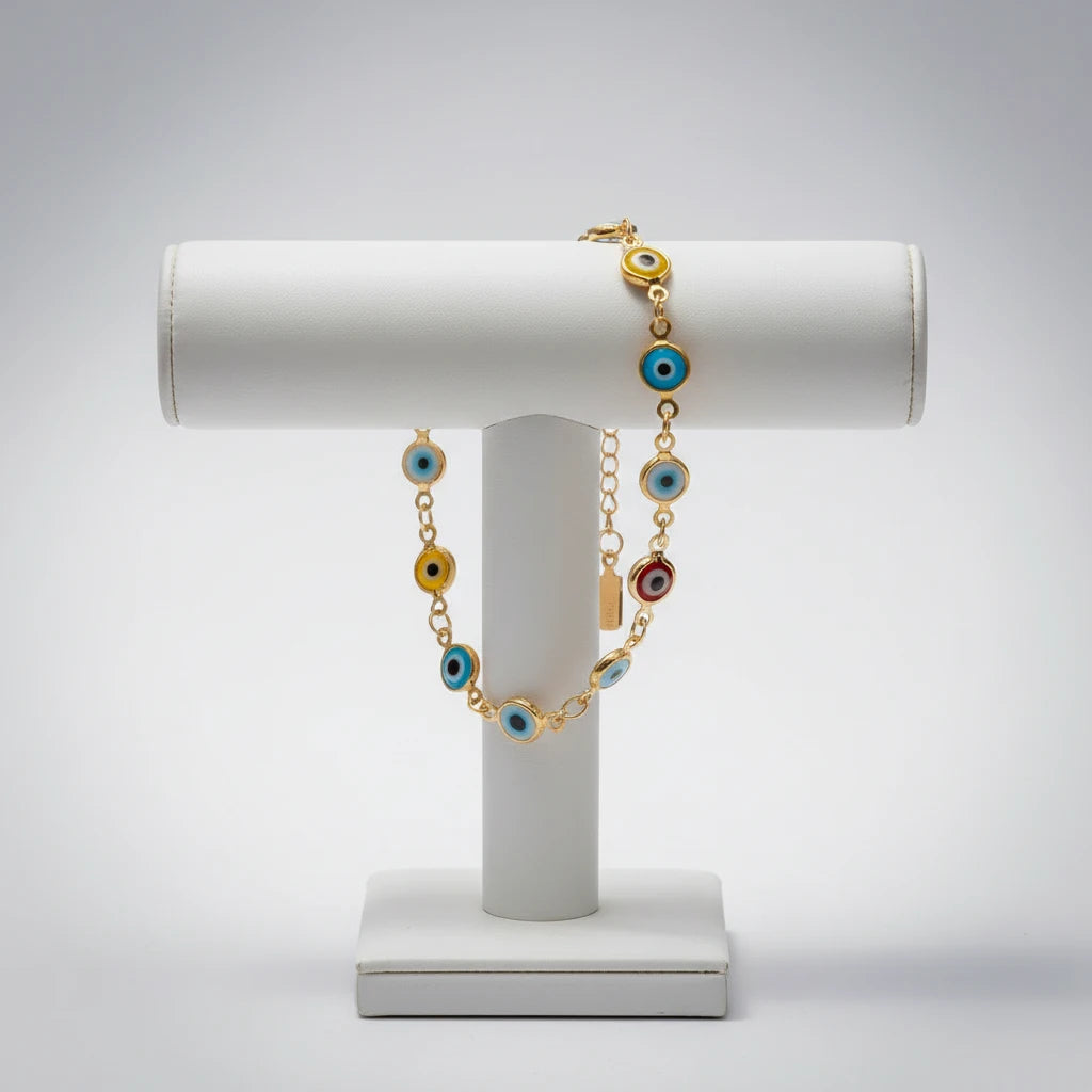 Studio display of the Evil Eye Charm Bracelet draped over a white jewelry stand, emphasizing the gold chain and alternating blue, yellow, red, and turquoise evil eye charms in a clean, minimalist setting | Oria Jewel