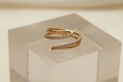 Macro product close-up of the Gold CZ Wrap Ring on a frosted acrylic cube, highlighting the elegant spiral wrap shape and pavé CZ detail against a clean neutral background | OriaJewel