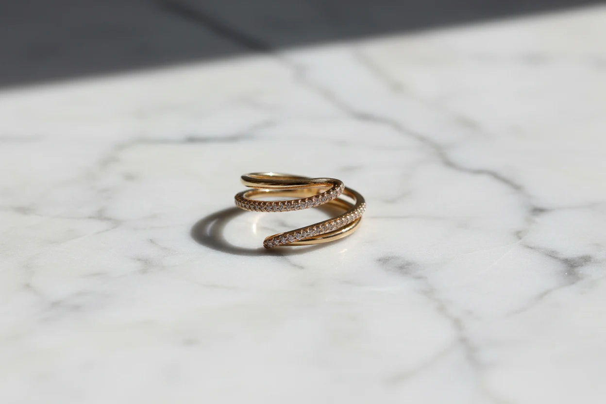 Minimal marble surface product shot of the Gold CZ Wrap Ring in direct sunlight, showing the layered wrap design, CZ sparkle, and a crisp shadow for a premium look | OriaJewel