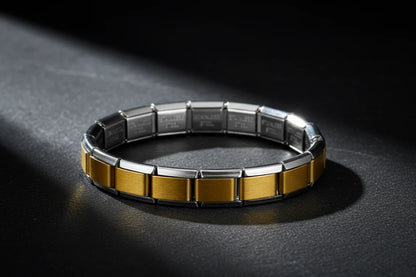 Dramatic studio close-up of Gold Center Stainless Steel Stretch Bracelets resting in a circular shape on a dark textured surface, with a spotlight highlighting the contrast between the brushed gold center links and polished silver edges | Oria Jewel
