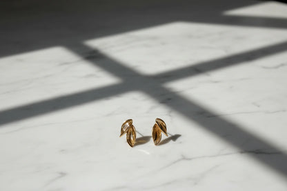 Gold Double Leaf Stud Earrings on marble surface with window light shadows | OriaJewel