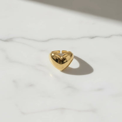 Gold Heart Open Ring on white marble surface with soft natural sunlight and a clean shadow, showing the puffy heart shape and open adjustable band. | OriaJewel