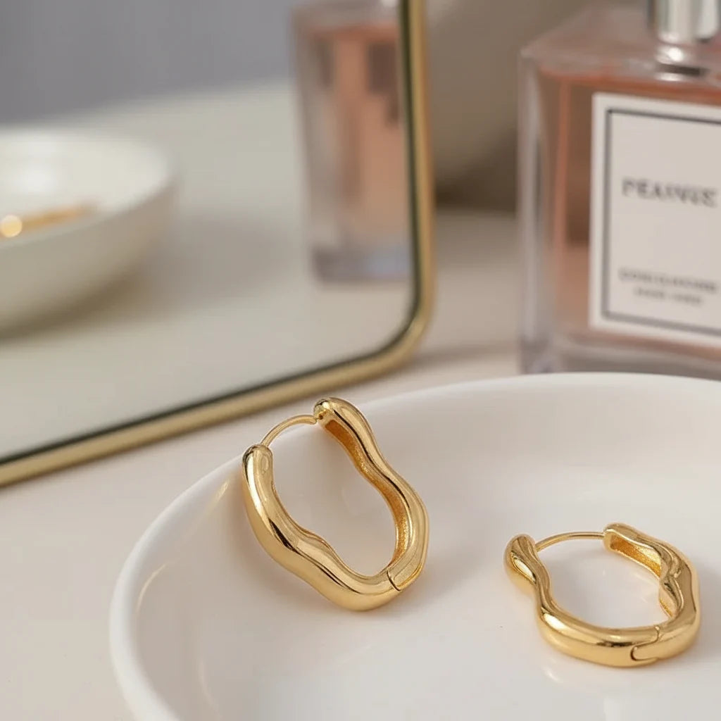 Gold Huggie Hoop Earrings close-up on white dish with vanity mirror and perfume | OriaJewel
