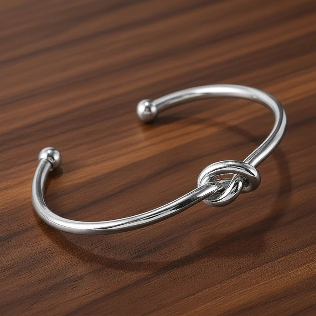 Sleek silver-tone version of the Gold Knot Cuff Bracelet on a wooden surface, showing the minimalist knot and rounded open ends for an adjustable fit | Oria Jewel