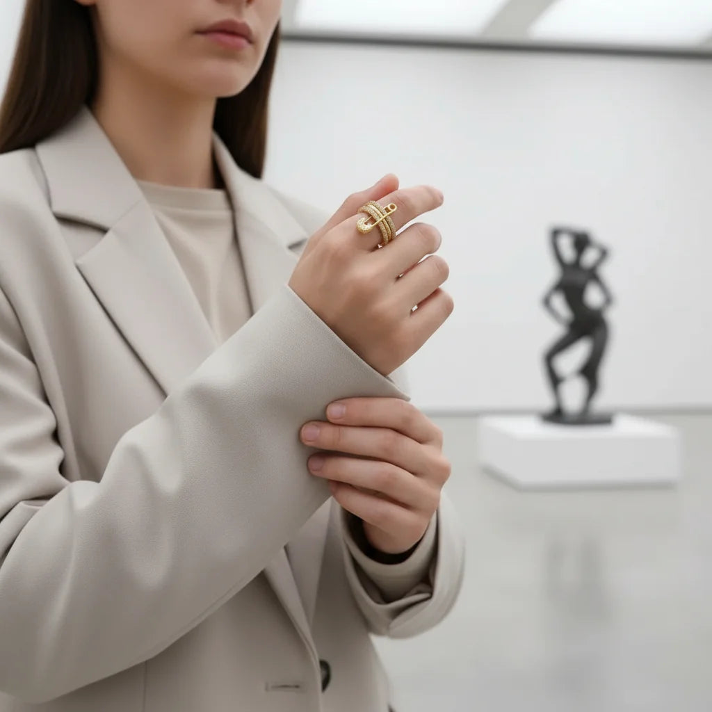 Gold Safety Pin Ring worn with a neutral blazer in a modern gallery setting, close-up hand pose, clean background blur, spotlight on the pavé safety pin detail and heart charm | OriaJewel