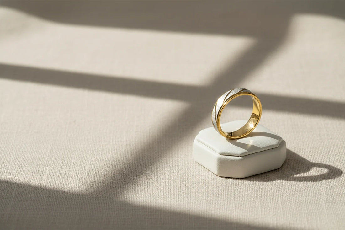 Minimal lifestyle product shot of a Gold Silver Two Tone Band Ring standing on a white ring box, warm window-light shadows on textured fabric | OriaJewel