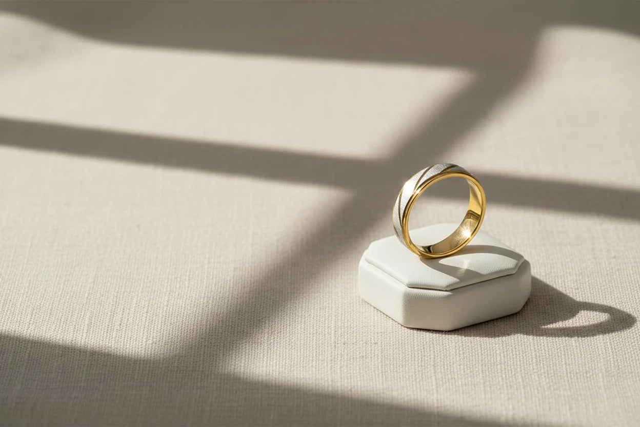 Minimal lifestyle product shot of a Gold Silver Two Tone Band Ring standing on a white ring box, warm window-light shadows on textured fabric | OriaJewel