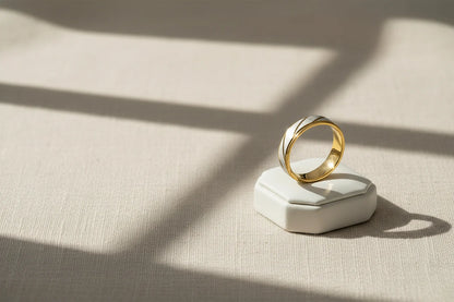 Minimal lifestyle product shot of a Gold Silver Two Tone Band Ring standing on a white ring box, warm window-light shadows on textured fabric | OriaJewel