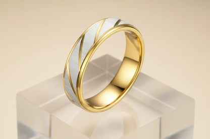 Studio hero shot of a Gold Silver Two Tone Band Ring on a clear acrylic block, brushed silver center panel with diagonal gold lines, beige gradient background | OriaJewel