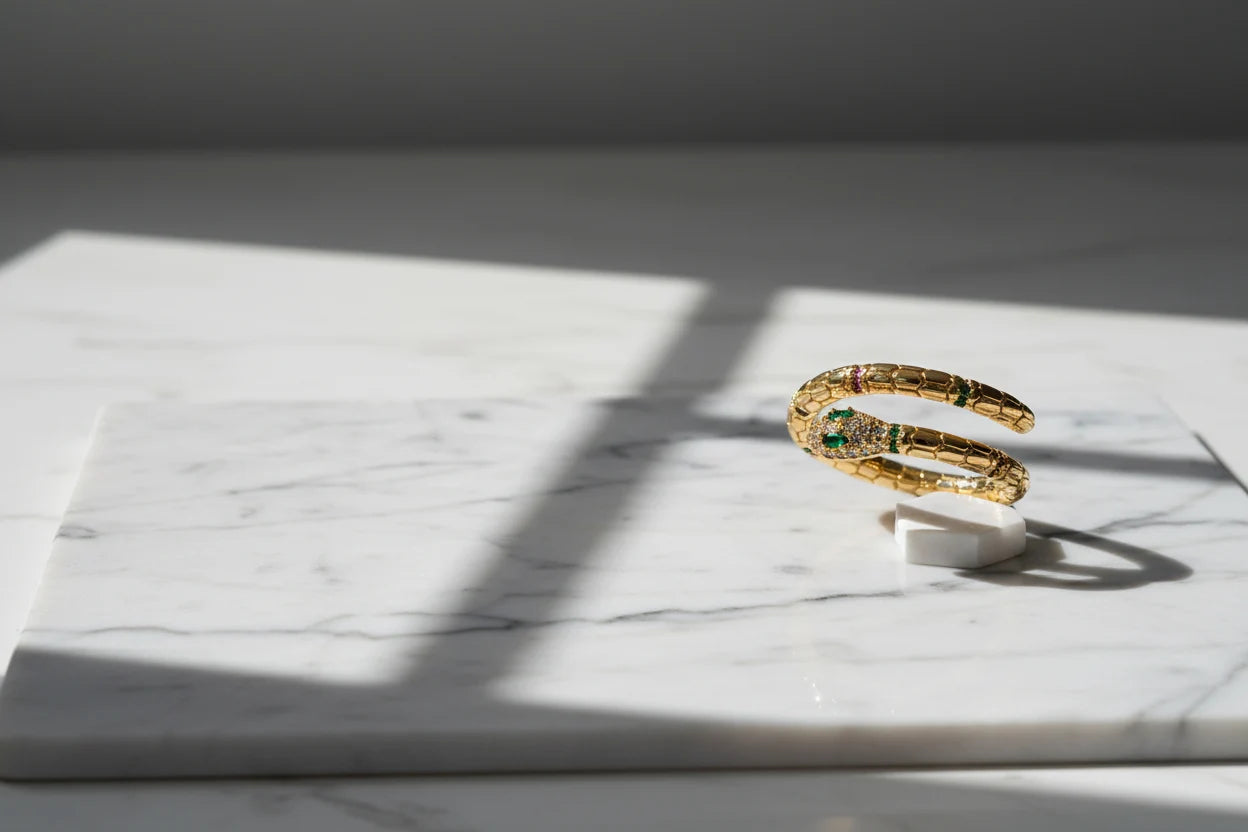 Gold Snake Wrap Ring displayed on white marble under window-grid shadows, side view highlighting the open wrap coil and sparkling snake head with green accents | OriaJewel