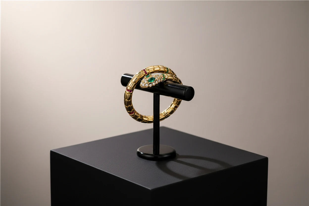 Gold Snake Wrap Ring mounted on a black jewelry stand on a matte pedestal, showcasing the statement snake wrap silhouette and jeweled head in dramatic studio lighting | OriaJewel