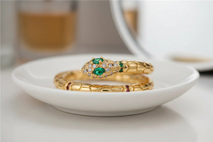 Gold Snake Wrap Ring macro on a white dish with soft bokeh background, detailed view of the pavé crystal snake head and emerald-green eyes on a gold coiled band | OriaJewel