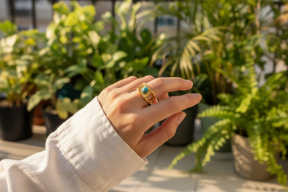 Gold Turquoise Adjustable Open Ring worn on a hand outdoors in warm sunlight, surrounded by green plants, highlighting the turquoise stone and textured sunburst face on the gold adjustable band | OriaJewel