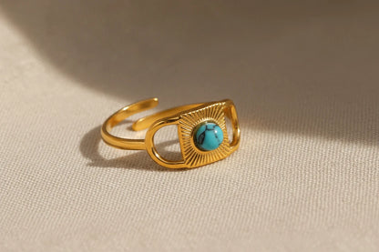 Gold Turquoise Adjustable Open Ring macro on textured beige fabric, detailed view of the turquoise cabochon and engraved sunburst pattern framed by open geometric gold sides | OriaJewel