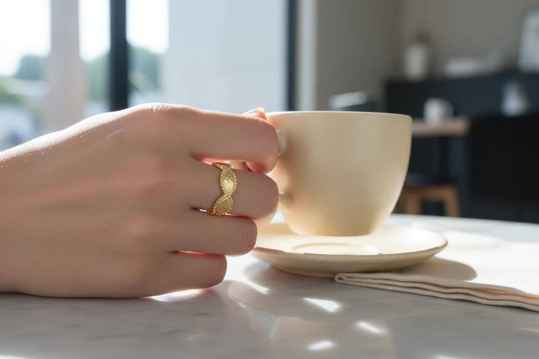 Gold beaded marquise ring on a hand holding a cream coffee cup over a marble table, soft morning sunlight and blurred cafe background | OriaJewel