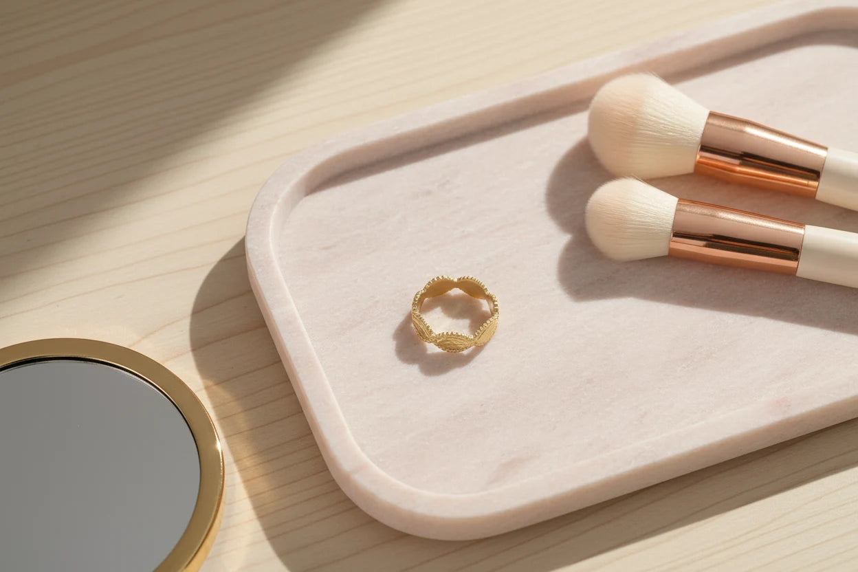 Gold beaded marquise ring displayed on a pale stone tray next to soft makeup brushes and a round mirror, minimal beauty flat-lay in natural light | OriaJewel