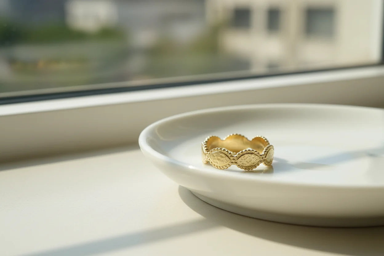 Gold beaded marquise ring resting on a white plate by a sunlit window, airy minimal scene with gentle reflections and soft background blur | OriaJewel