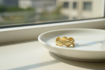 Gold beaded marquise ring resting on a white plate by a sunlit window, airy minimal scene with gentle reflections and soft background blur | OriaJewel