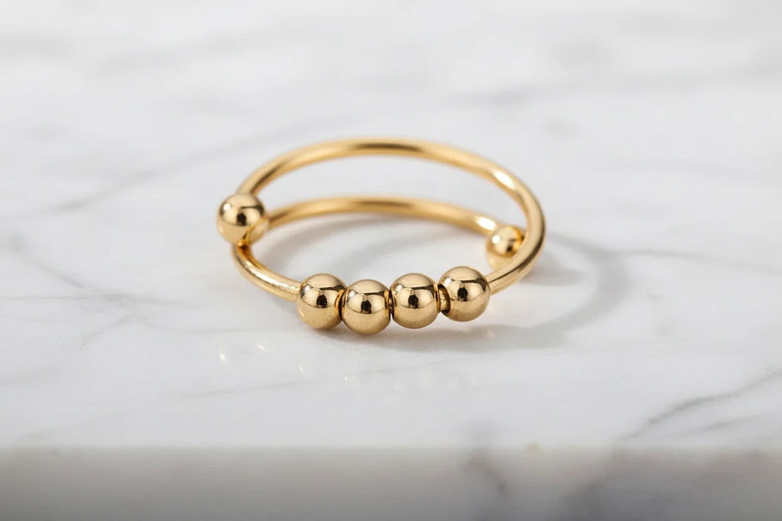 Minimal product close-up of the Gold beaded stackable ring on a light marble surface, highlighting the open double band shape and bead row with soft, diffused lighting | OriaJewel