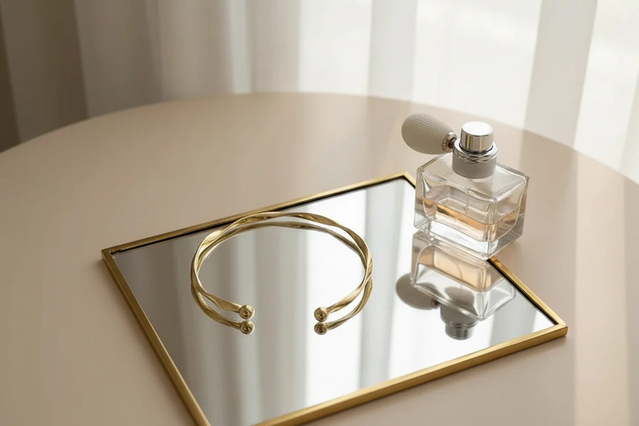 Flat lay of a Gold twisted cuff bracelet resting on a framed mirror next to a vintage-style perfume bottle, creating a soft feminine aesthetic | Oria Jewel