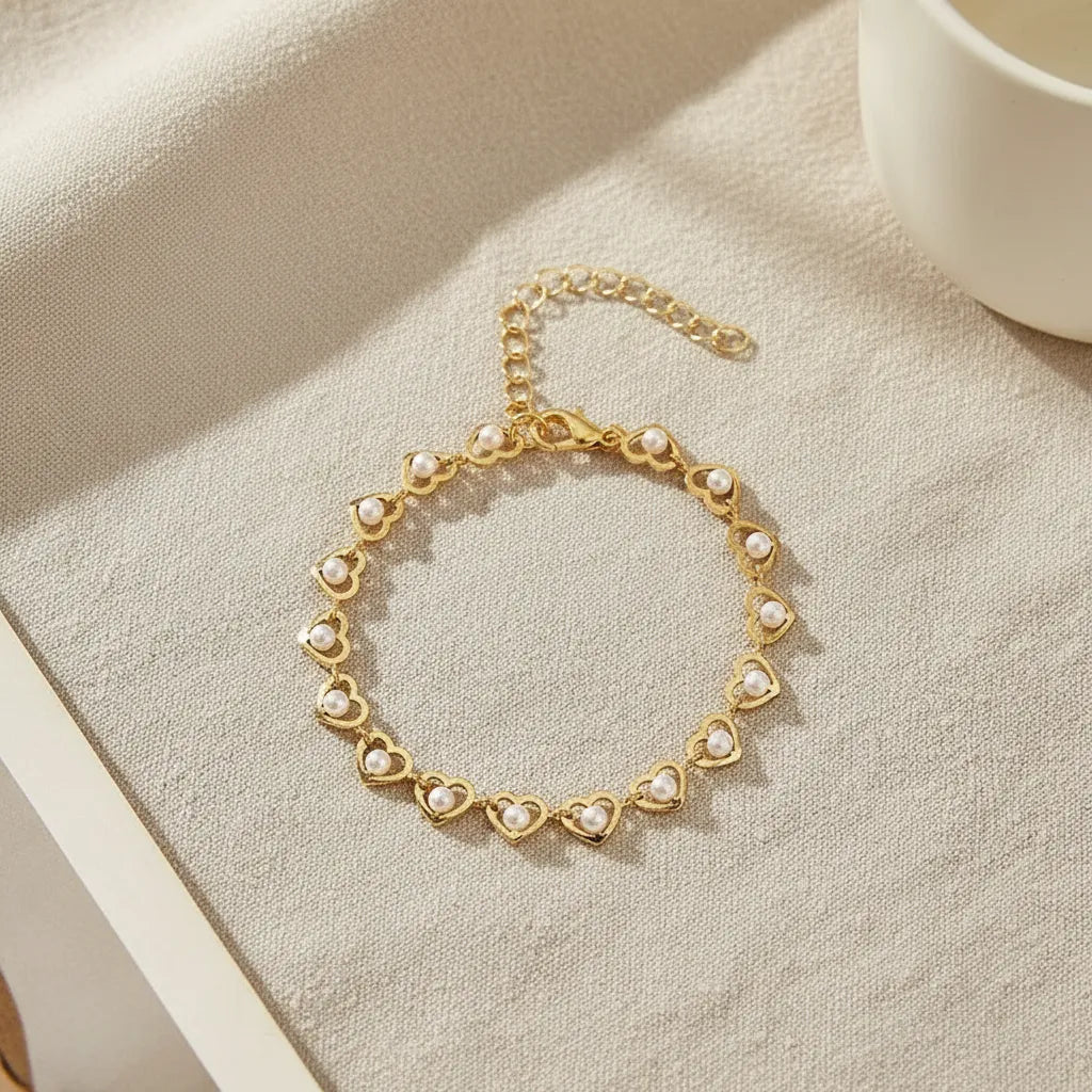 Golden Pearl Heart Chain Bracelet laid in a perfect circle on a neutral linen surface, softly lit to showcase the repeating heart-and-pearl design and delicate chain extender | Oria Jewel