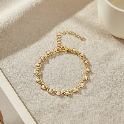 Golden Pearl Heart Chain Bracelet laid in a perfect circle on a neutral linen surface, softly lit to showcase the repeating heart-and-pearl design and delicate chain extender | Oria Jewel