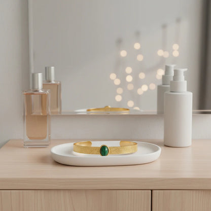 Green Gemstone Cuff Bracelet resting on a white ceramic tray in front of a mirror on a light wood vanity, surrounded by minimal perfume bottles and skincare pumps, creating a clean, feminine dressing-table scene | Oria Jewel