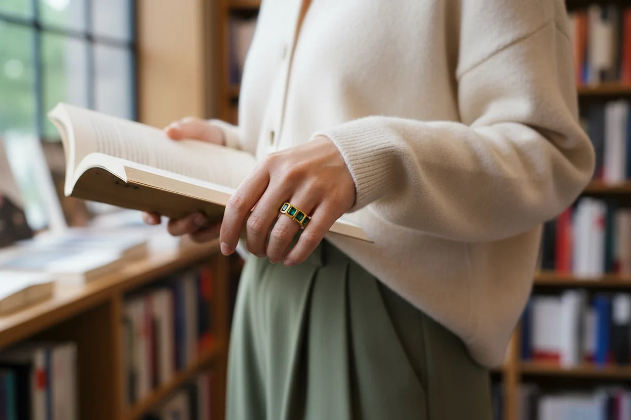 Green stone band ring shown while holding an open book indoors, clean lifestyle styling with soft window light and crisp focus on the rectangular green stones | OriaJewel