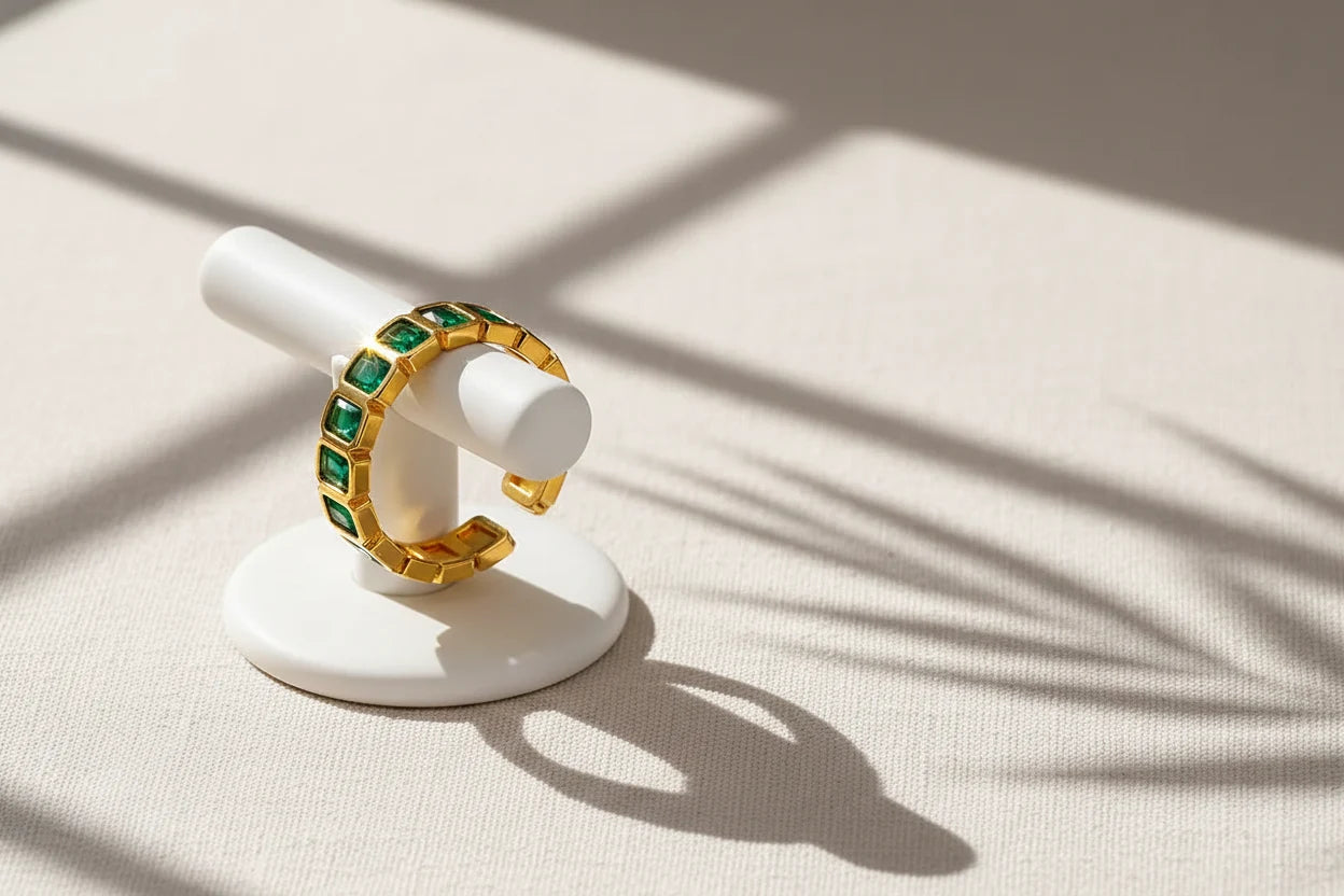 Green stone band ring displayed on a white ring stand with dramatic window-shadow lines, minimalist studio look emphasizing the open band shape and green stones | OriaJewel