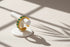 Green stone band ring displayed on a white ring stand with dramatic window-shadow lines, minimalist studio look emphasizing the open band shape and green stones | OriaJewel