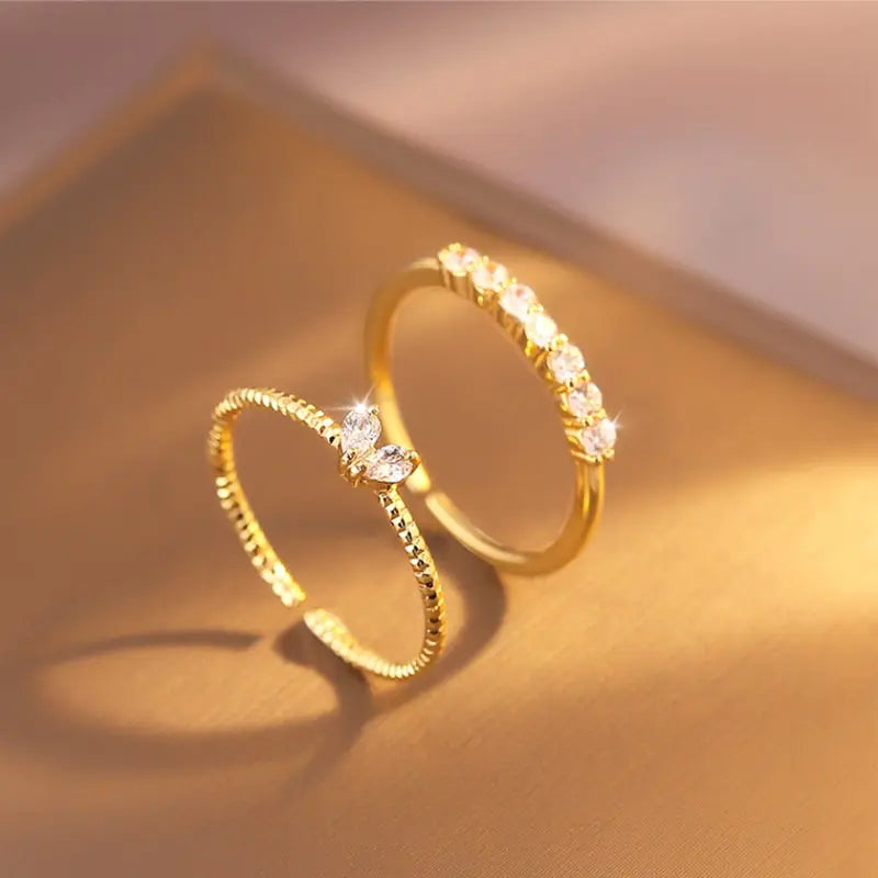 Luna Dainty Stack Ring Set product styling on a warm neutral surface with soft glow, highlighting the open adjustable marquise ring paired with the slim crystal band ring | OriaJewel