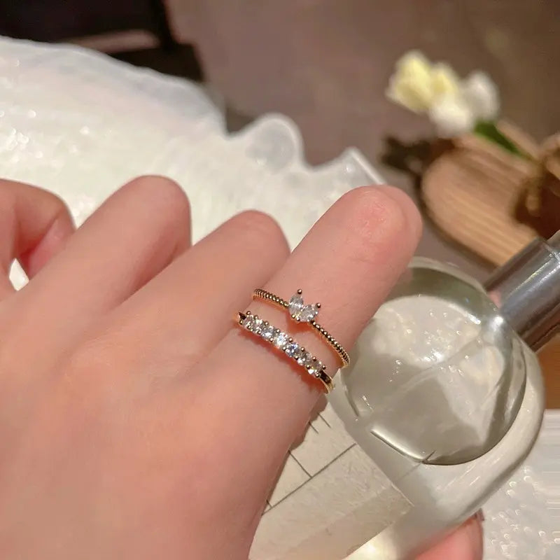 Luna Dainty Stack Ring Set worn stacked on the finger beside a clear perfume bottle, showing the dainty gold bands and sparkling stones in a cozy vanity-style scene | OriaJewel